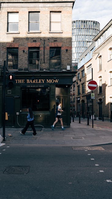 A street corner in Shoreditch Old Street displaying a small cafe with a rustic wooden sign reading 'PAUSE' above the entrance, which features a large glass window revealing a cozy interior illuminated
